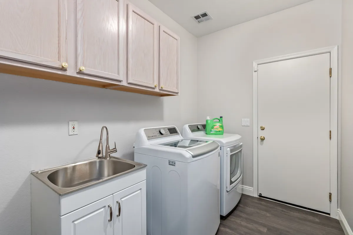 A bright, organized laundry room equipped with modern washing machines, a utility sink, and overhead cabinets for storage. The space is tidy and designed for efficiency, reflecting a well-thought-out amenity that adds everyday comfort.