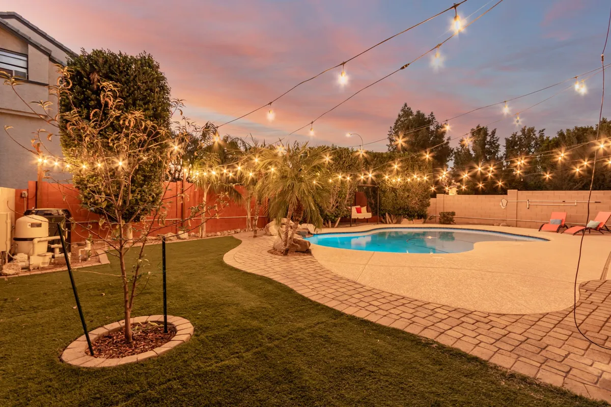 This exterior image showcases a sparkling pool framed by string lights, a well-kept lawn, and a covered patio area. The scene is festive and inviting, ideal for families wanting a backyard space to swim, dine, and play together.