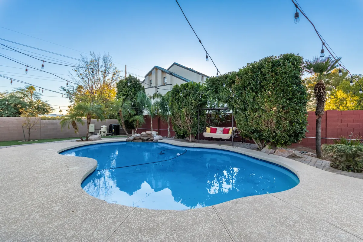 This inviting scene features a hammock beside a sparkling pool, surrounded by lush plants and illuminated by strands of twinkling string lights. The space blends opportunities for relaxation, swimming, and entertaining in a tranquil, private setting.