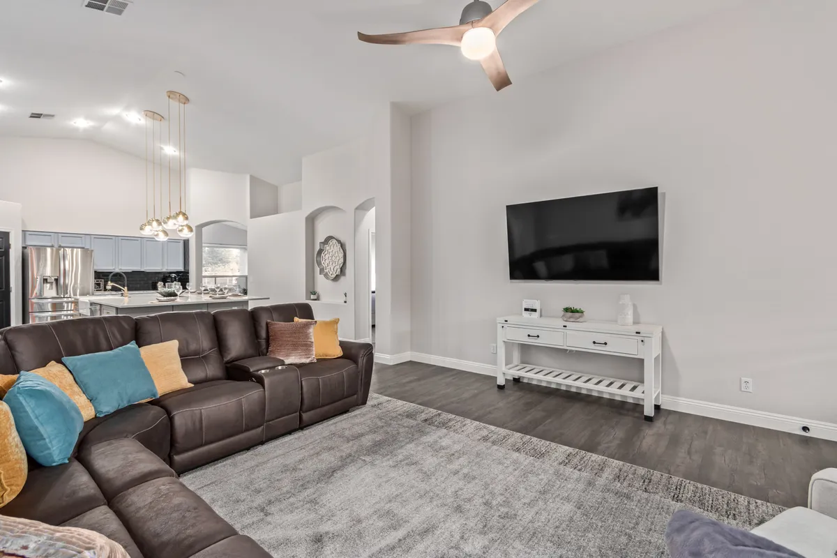 A contemporary family room with a leather sectional sofa, coffee table, television, ceiling fan, and stylish pendant lights. The setup encourages relaxation, movie nights, and lively family discussions, bringing warmth and modern comfort to the space.