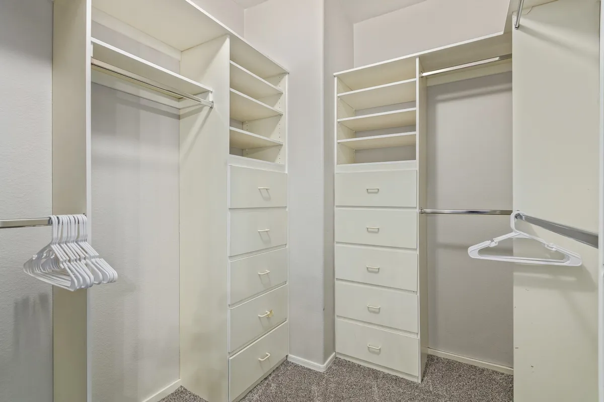 A thoughtfully organized custom walk-in closet with hanging racks, drawer units, and shelves. The space is neat and perfectly arranged for storing clothing and accessories, evoking a sense of order and luxury.