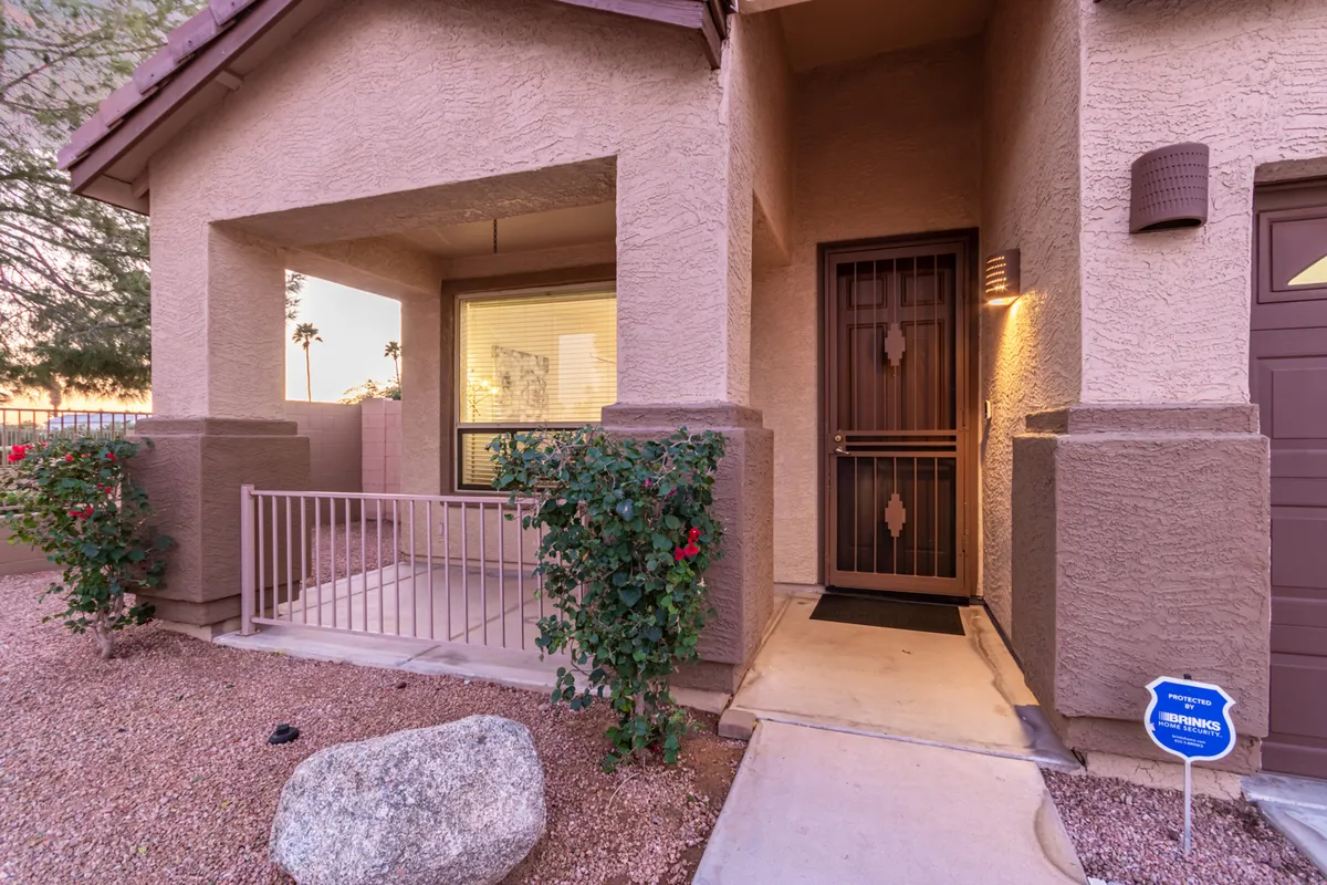A charming view of the front door framed by blooming rose bushes and a stone pathway, the image conveys a tranquil, neighborly atmosphere. The porch space hints at relaxed mornings and a sense of belonging in the local neighborhood.