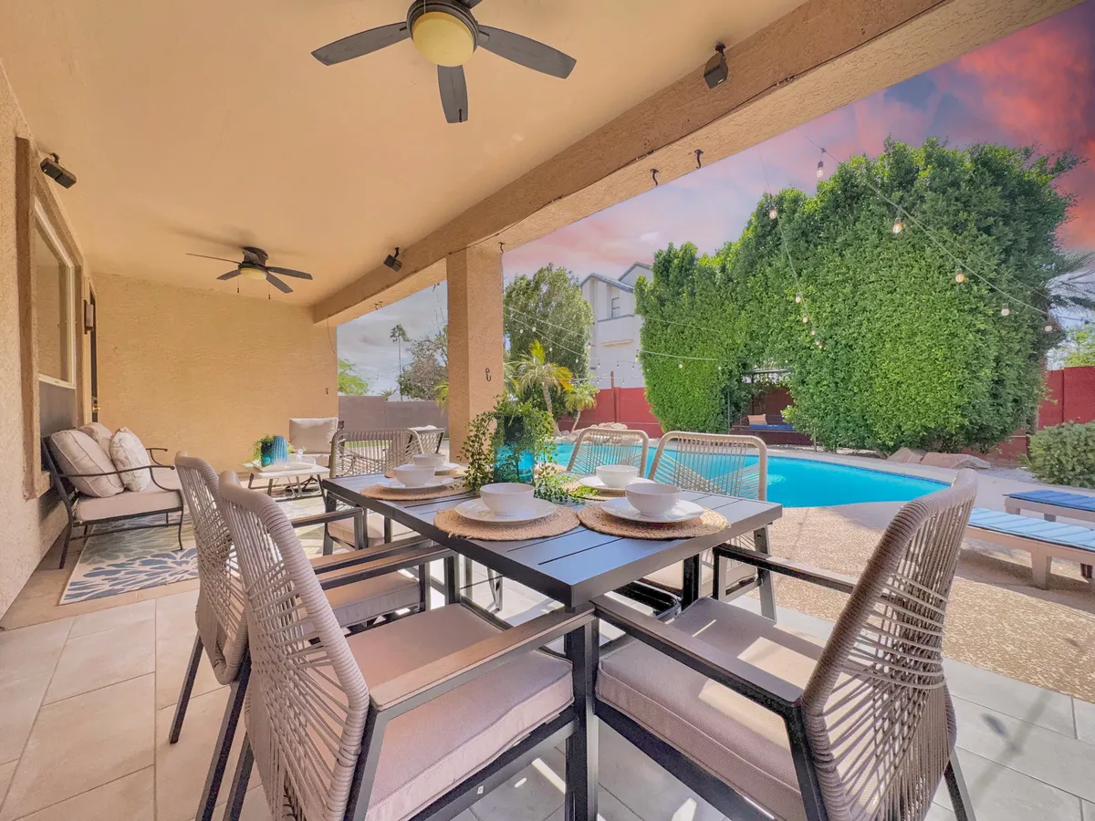 A view of an outdoor dining table set for a meal, with a swimming pool and inviting seating area in the background, surrounded by lush plants. The image radiates a welcoming mood for group meals and poolside relaxation.