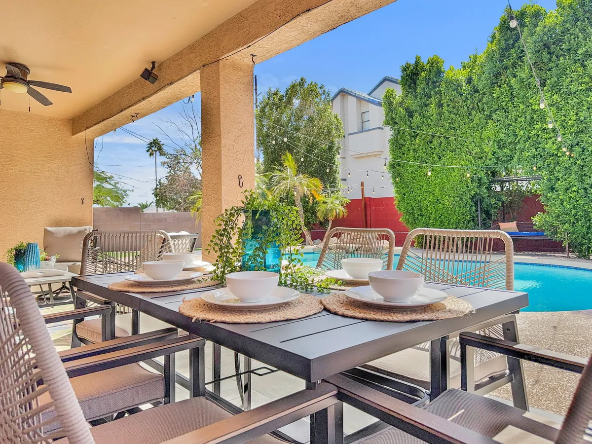 This image captures an outdoor dining table set beside the pool, surrounded by lush greenery and decorative lanterns. The setup is ideal for sunset or alfresco dining, with the pool offering a scenic backdrop for meals and gatherings.